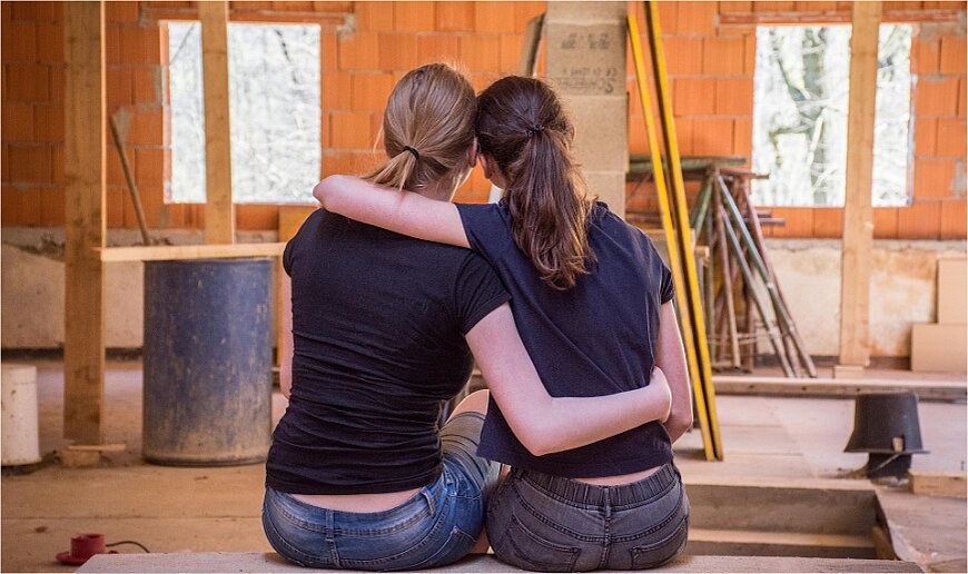 Zwei Freundinnen umarmen sich in der neuen Wohnung/Baustelle